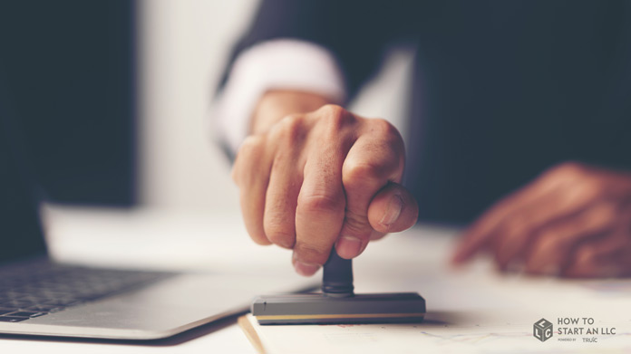 A closeup of a man’s hand stamping a certificate of good standing on a desk