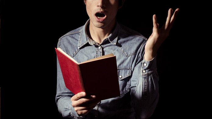 A man reading aloud from a red book