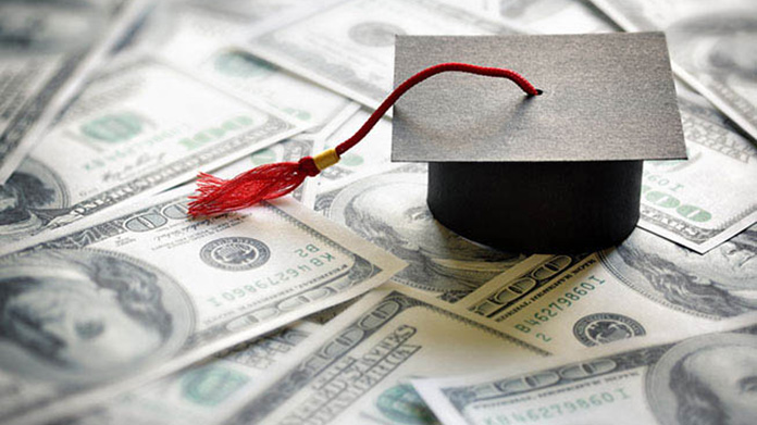 A small graduate cap on top of hundred-dollar bills