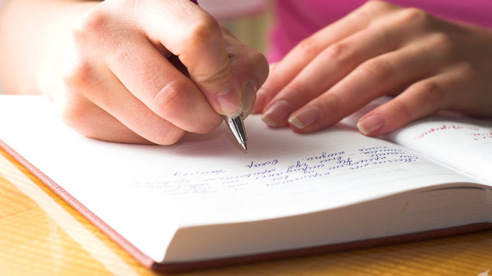 A pair of hands writing in a journal