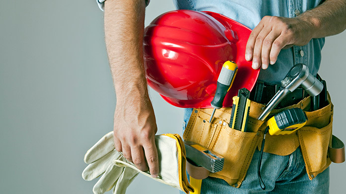 A man with a toolbelt holding gloves and a hard hat