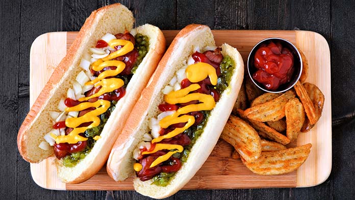 Two hot dogs, chips, and ketchup on a serving board