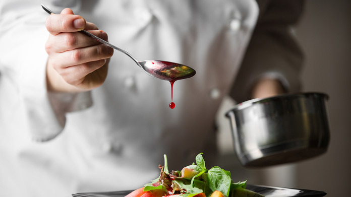 A chef drizzling a salad with dressing