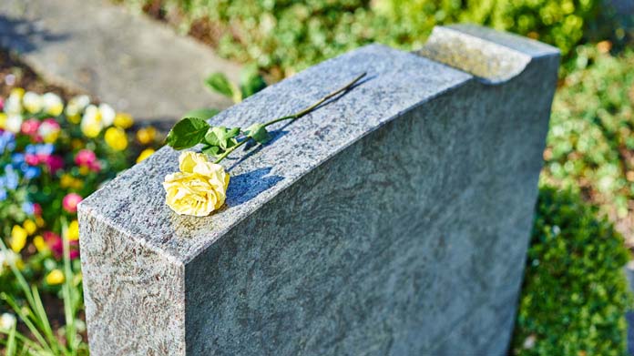 A yellow rose laying on a headstone