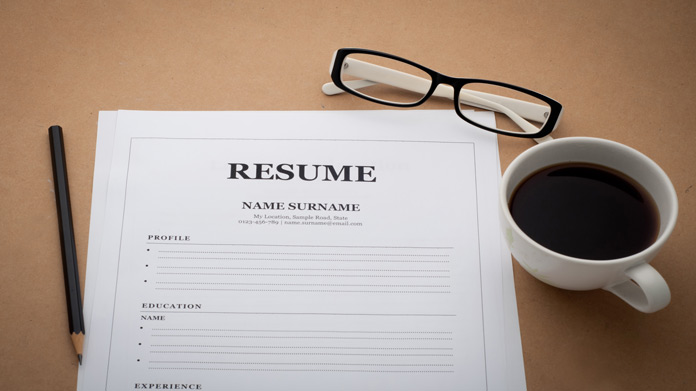 A resume, pencil, glasses, and mug of coffee on a table