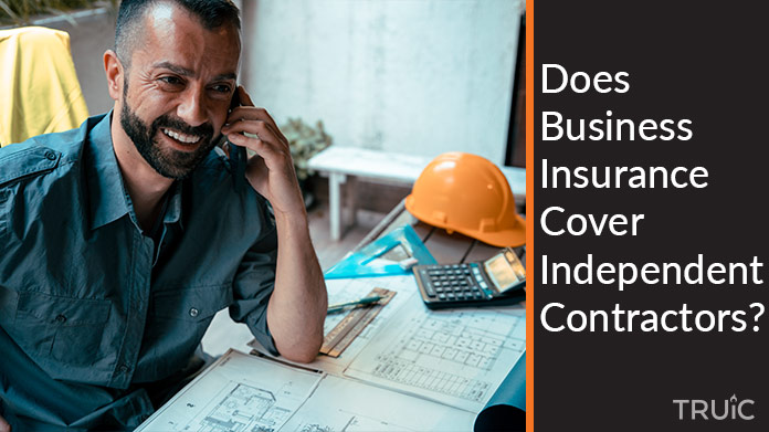 Man on a cellphone with blueprints and a hard hat next to him.