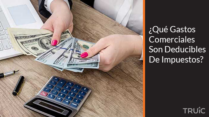 Una emprendedora contando su dinero en su oficina, utilizando su calculadora y computadora.