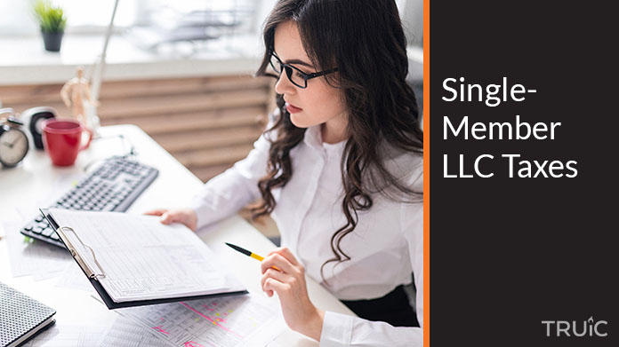 A businesswoman sits at a desk with a clipboard filing taxes for a single member LLC